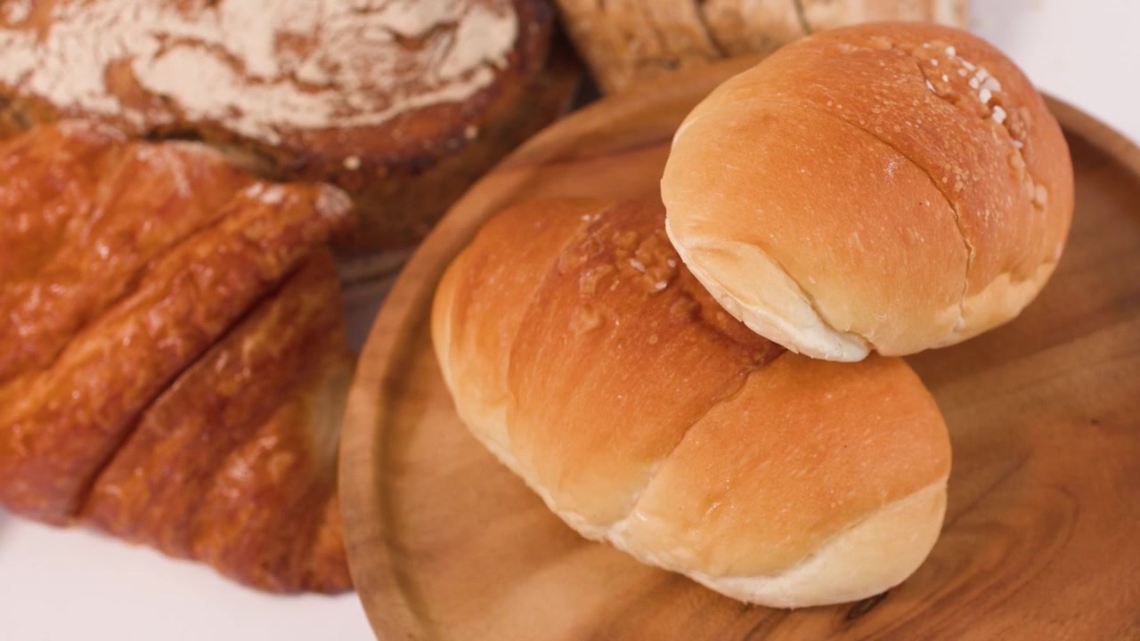 Roterende nærbillede af surdej, croissanter og boller på en træplade med blød belysning