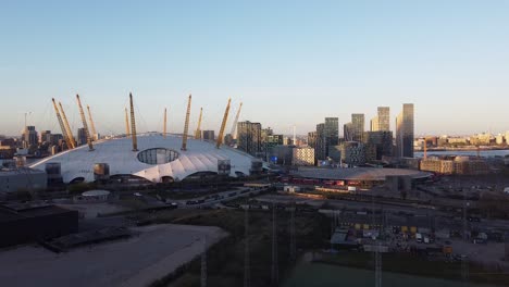 Luftaufnahme,-Die-Die-O2-Arena-Mit-Der-Skyline-Von-Canary-Wharf-Während-Des-Sonnenuntergangs-Im-Hintergrund-Zeigt