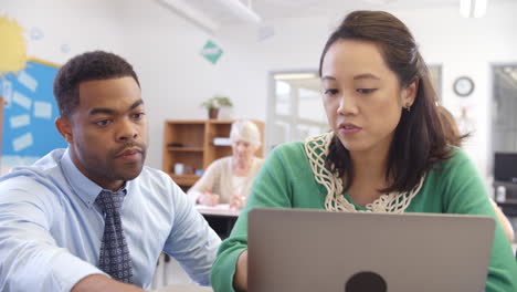 Teacher helps woman using laptop at an adult education class