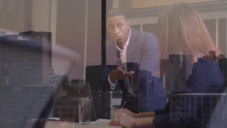 Animation-of-multiracial-coworkers-discussing-reports-over-laptop-at-office-over-aerial-view-of-city