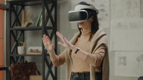 young woman architect in office in virtual reality helmet with hands commits movements simulating a graphic interface work.