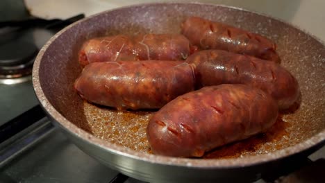 five big and bright red chorizo sausages being cooked in a pan