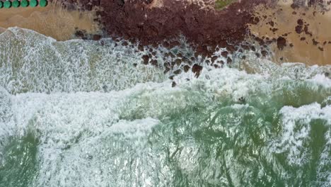 Toma-Aérea-De-Pájaros-Teledirigidos-De-Pequeñas-Olas-Que-Se-Estrellan-Contra-Las-Rocas-En-La-Famosa-Playa-Tropical-Del-Amor-En-Pipa-Brasil-En-Río-Grande-Do-Norte-Con-Arena-Dorada,-Agua-Turquesa-Cálida-Y-Sombrillas-Coloridas