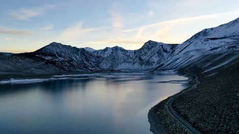 scenic coastal mountain road with snowy peaks in horizon, aerial drone view