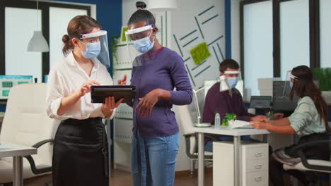 worker with face mask discussing with black woman holding tablet