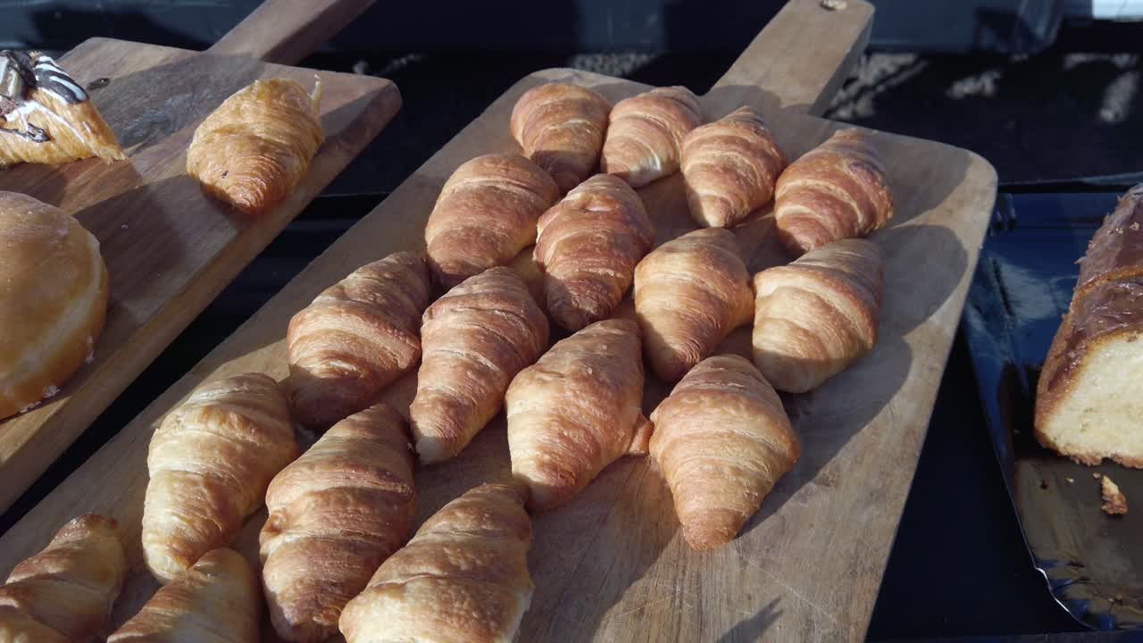 Golden brown croissants are neatly arranged on wooden boards, alongside other pastries like donuts and slices of pound cake, possibly at a breakfast buffet or bakery display