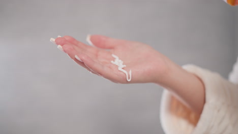 woman pours liquid cream for face into hand in shower. creamy facial emulsion drips onto female hand in spacious room with blurred background