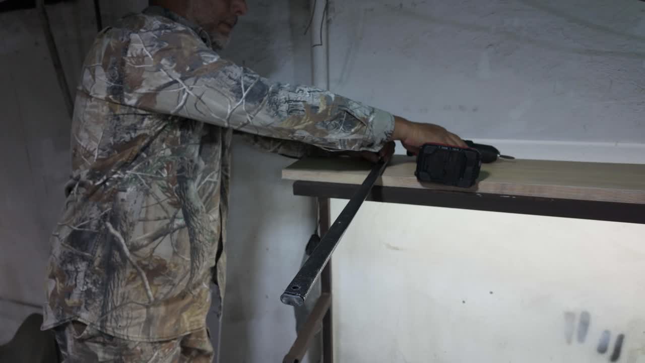 A skilled worker focuses on his craftsmanship, using a cordless drill to create an opening in metal. The workshop is well-lit with tools organized around him, showcasing diligence and expertise.