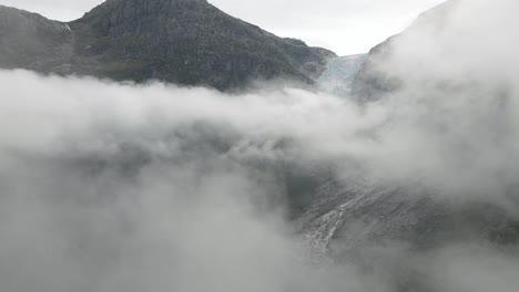 一座岩石山矗立在云彩中, 坐落在宏伟的冰川上, 空中无人机拍摄