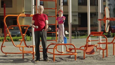 Granddaughter-and-grandfather-doing-fitness-exercises-with-dumbbells.-Senior-man-with-child-kid-girl