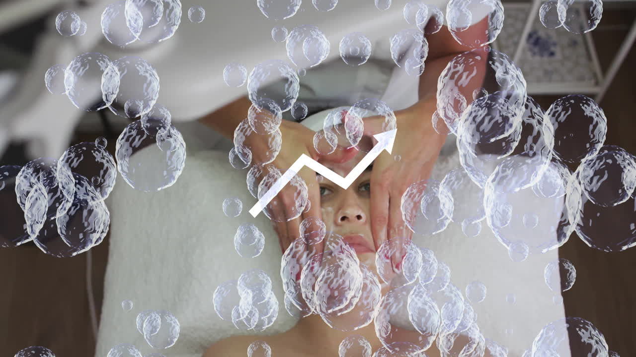 female therapist hands massaging client face in spa, showing floating bubbles and upward arrow