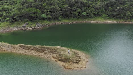 Male-Controlling-and-Flying-Drone-at-Danao-lake-in-San-Juan,-Southern-Leyte,-Philippines,-Aerial,-pullback