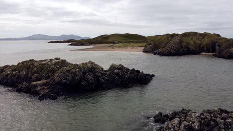 Vista-Aérea-Ynys-Llanddwyn-Island-Anglesey-Sendero-Costero-Con-Montañas-Snowdonia-Bajo-Vuelo-A-Través-Del-Mar-Irlandés