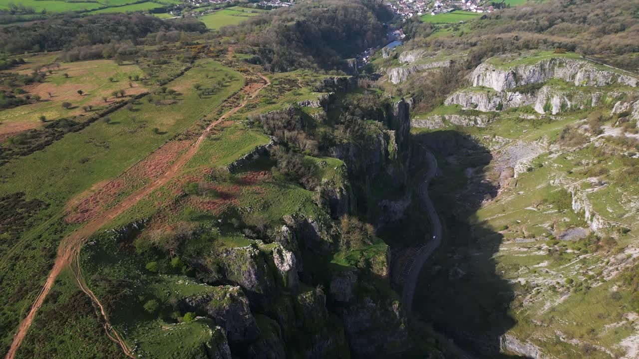 Backward aerial shot flying over Cheddar Gorge, revealing dramatic cliffs and roads.