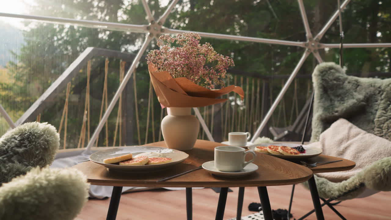 desayuno en la terraza de vidrio de la cabaña de glamping. mesa baja emparejada con sillones esponjosos crea una atmósfera tranquila para descansar con vistas impresionantes. mañana perfecta