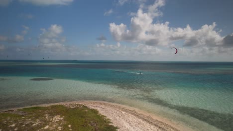 Toma-Aérea-De-Un-Kitesurfista-Con-Una-Cometa-Roja-En-Cayo-Vapor,-Aguas-Turquesas-Bajo-Un-Cielo-Soleado