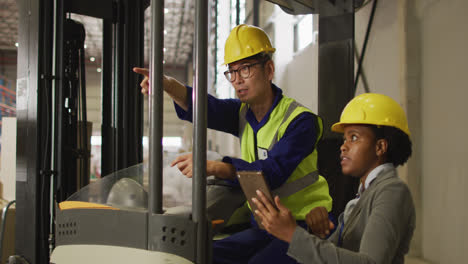 Diverse-male-and-female-workers-wearing-safety-suits-and-using-tablet-in-warehouse