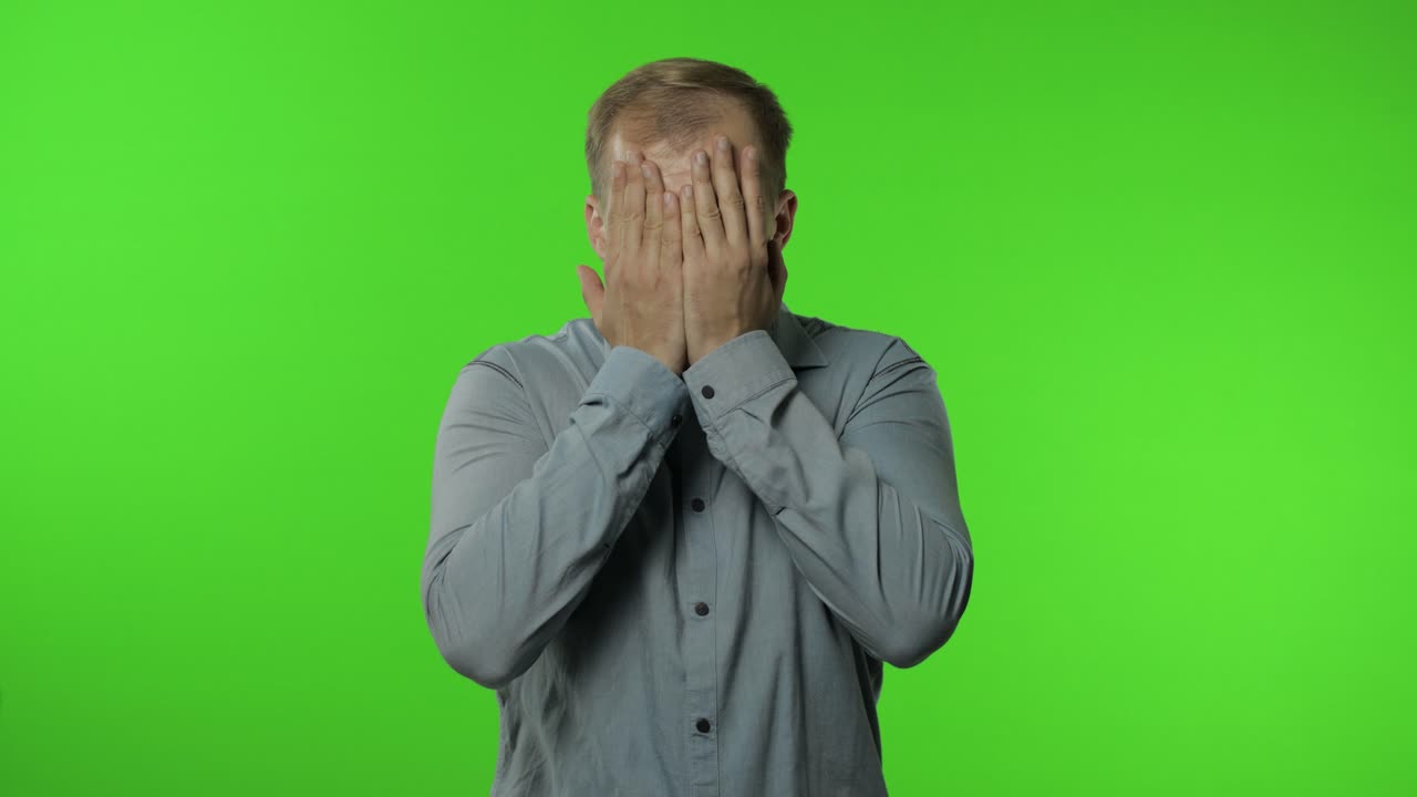 Shy guy scared to watch. Man covering eyes with hands and looking cautiously curious at camera