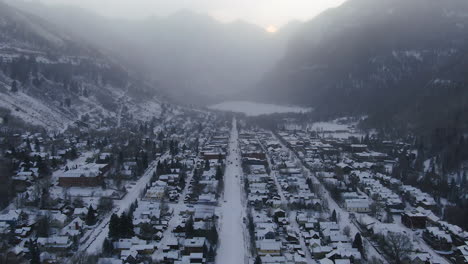 Vista-Aérea-De-Drones-De-La-Estación-De-Esquí-De-Montaña-De-Telluride-En-El-Centro-De-Colorado-Nieve-Fresca-Y-Niebla-Del-Paisaje-Montañoso-Escénico-Y-Edificios-Históricos-Camiones-Y-Automóviles-Mañana-Invierno-Movimiento-Panorámico-Hacia-Atrás