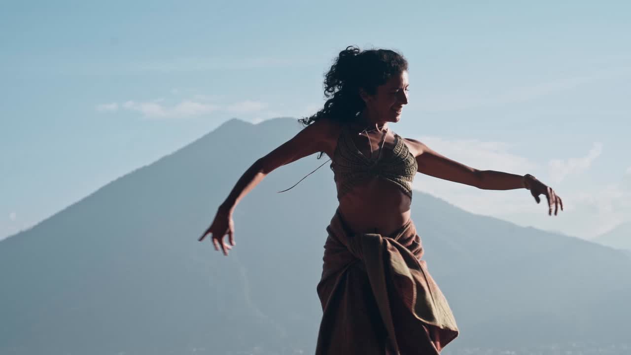 장엄한 자연 경관을 배경으로 행복한 기분으로 춤을 추는 긴 곱슬머리의 브루네트 여성