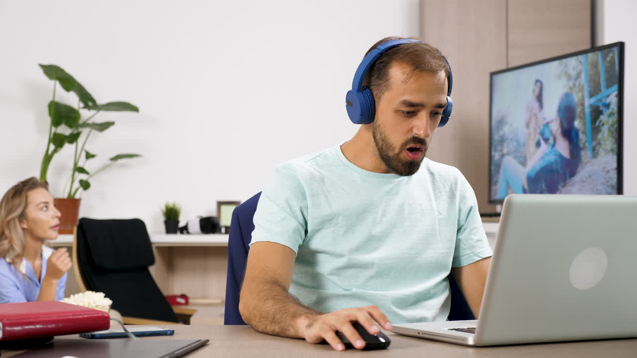 Man working on laptop while woman throws popcorn in the background