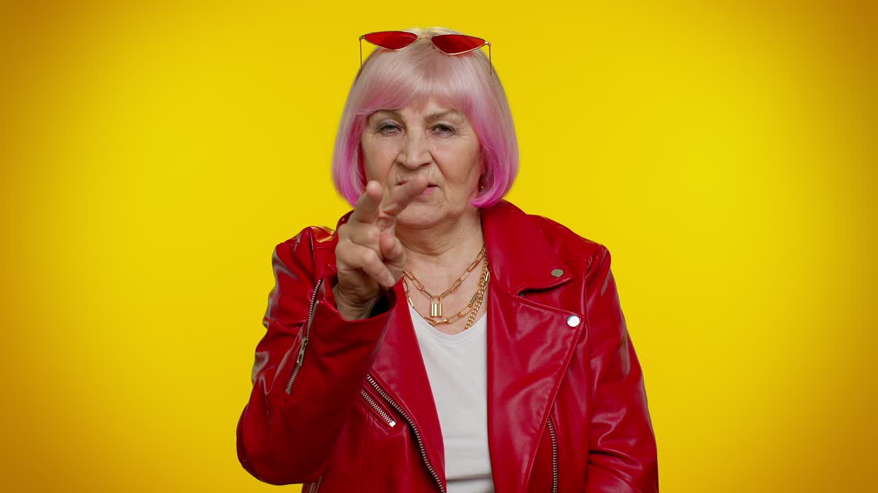 Anziana donna che indica i suoi occhi e la telecamera, mostrando il gesto "ti tengo d'occhio", spiando qualcuno.