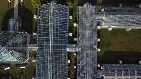 overhead rising drone shot of several glass greenhouses casting shadows on a sunny afternoon