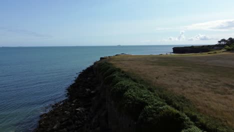 Traeth-Lligwy-idyllic-rocky-coast-shoreline-aerial-view-rising-across-green-pasture-on-rocky-cliffs-edge