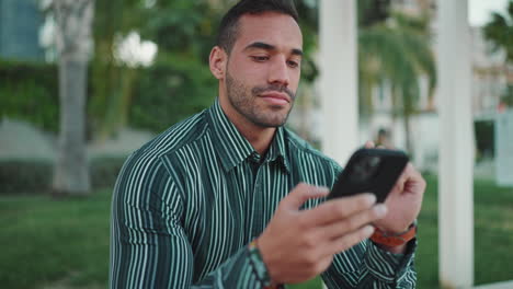 young man checking smartphone sitting in bench outdoors.