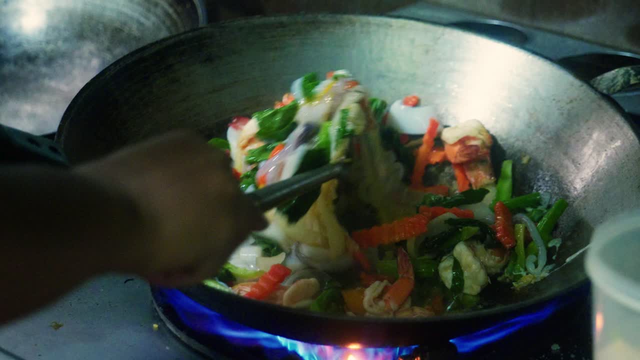 Filmato cinematografico di cucina in 4K di uno chef thailandese che cucina cibo thailandese in un wok in una cucina di ristorante in Thailandia