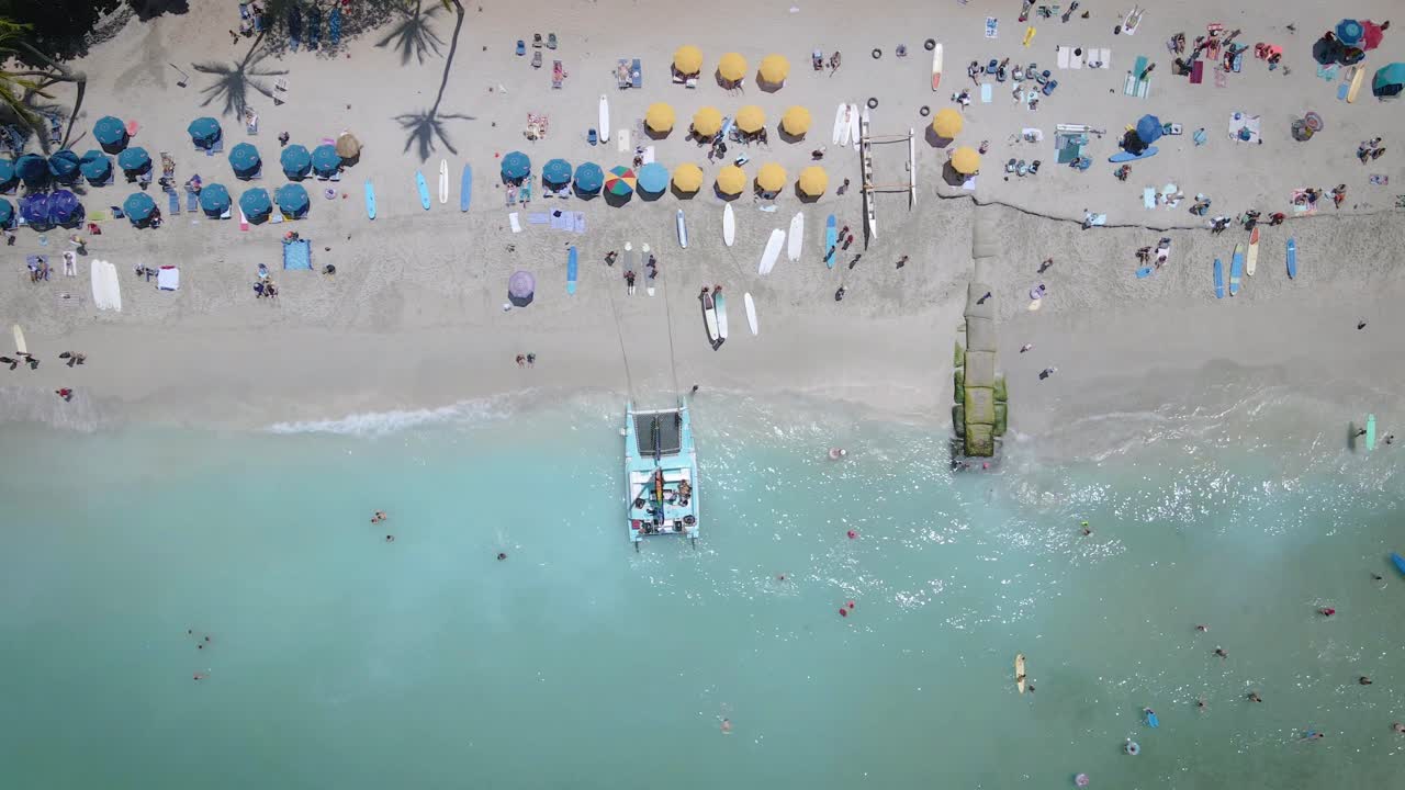 las imágenes aéreas capturan la belleza de una playa de arena blanca llena de paraguas de playa animadas, y la gente disfrutando de un baño refrescante