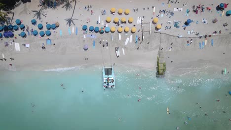 aerial footage captures the beauty of a white sandy beach filled with lively beach umbrellas, and people indulging in a refreshing swim