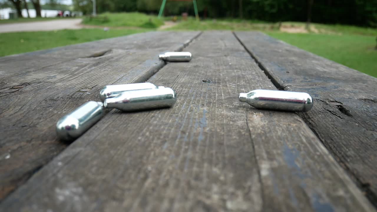 Multiple chrome nitrous oxide narcotics laughing gas drug cylinders falling on wooden park table