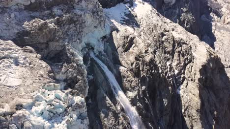 Acercamiento-Aéreo-A-Una-Cascada-De-Agua-De-Deshielo-De-Los-Glaciares-En-Verano-En-Los-Alpes-Suizos