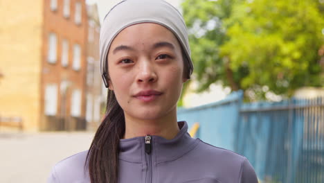 Close-Up-Portrait-Of-Young-Woman-Exercising-About-To-Run-Along-Urban-Street-Wearing-Wireless-Earbuds