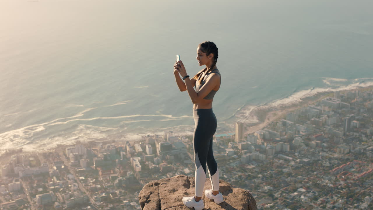 mulher jovem tirando fotos no topo da montanha usando smartphone compartilhando caminhadas aventura menina fotografando vista panorâmica com câmera de telefone celular de pé na borda do penhasco ao pôr do sol