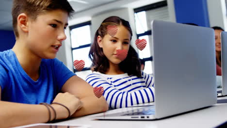 múltiples iconos de corazón rojo sobre un niño y una niña caucásicos usando una computadora portátil en la escuela
