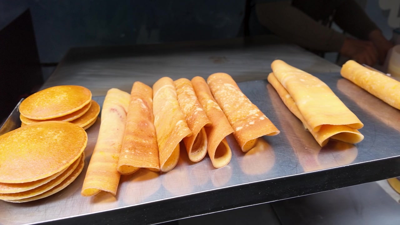 Jepretan jarak dekat seorang penjual yang memasak panekuk gulung tipis di atas wajan logam panas