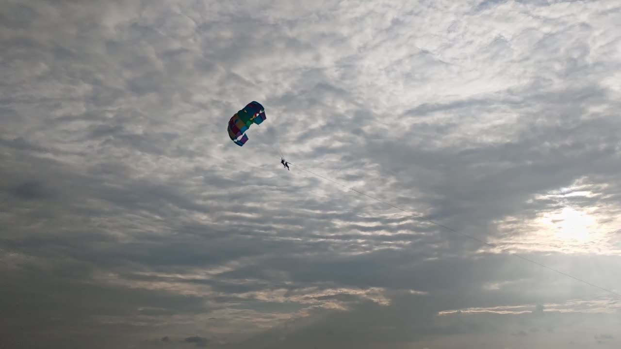 Silhouette shot of people with Parasailing in cloud sky and sun rays. day time, tracking shot, 4k
