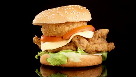 a crispy fried chicken burger with lettuce, tomato, cheese, and onion ring rotates smoothly against a glossy black background under bright studio lighting