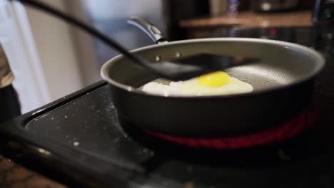 close-up static shot of a home-cook frying eggs over an induction cooktop using a rubber spatula