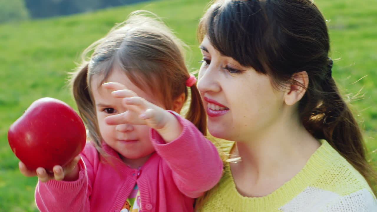 아이의 몸을 위한 건강한 식단 엄마와 딸이 푸른 잔디에서 사과를 가지고 즐겁게 놀고 있습니다