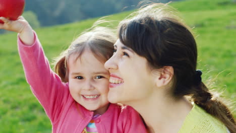 A-Healthy-Diet-For-A-Child's-Body-Mom-And-Daughter-Are-Playing-Fun-With-An-Apple-On-Green-Grass