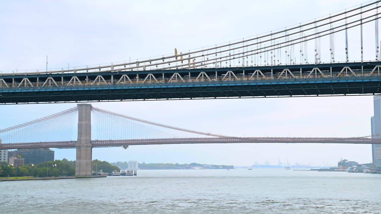 Long train moves by the Manhattan Bridge. Low angle view on the bridge from the riverscape on foggy day