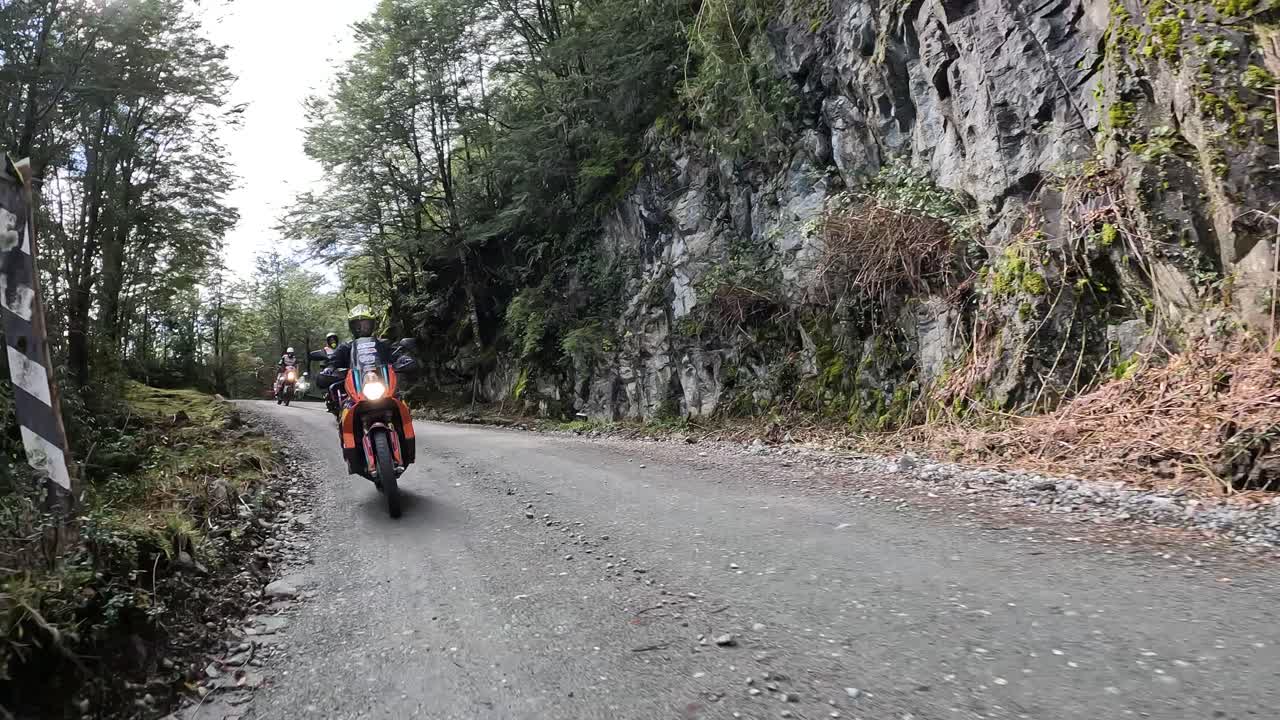 Group of motorcyclists riding on a gravel road surrounded by forests and rock walls. Chilean Patagonia