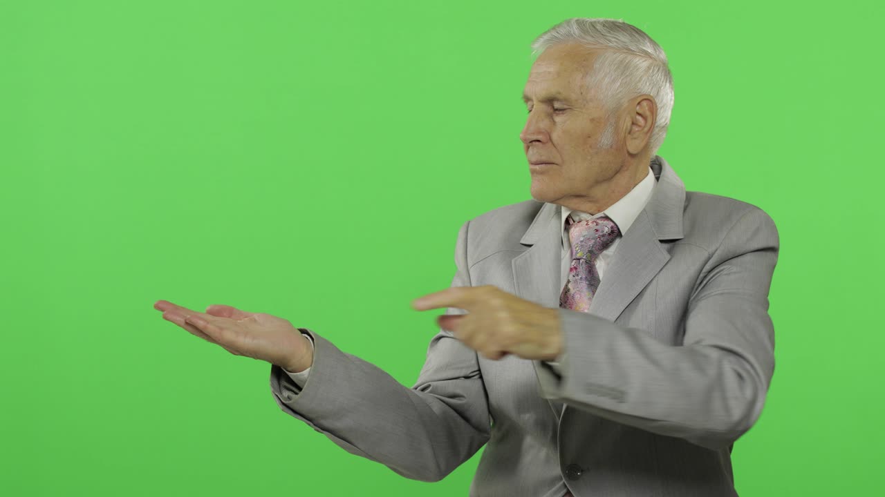 Elderly businessman points at something and thumb up. Old man in formal wear