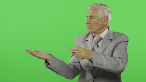 elderly businessman points at something and thumb up. old man in formal wear