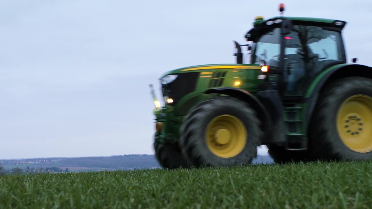 Contadino con trattore distribuisce semi sul suo campo. Ripreso a terra con una bella carrellata e un ampio paesaggio sullo sfondo
