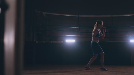 female boxer training in dark room with back light in slow motion. steadicam shot