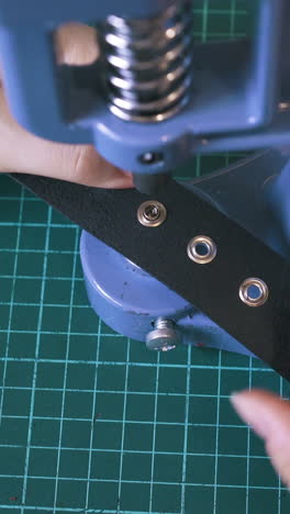 cu: professional girl tailor sets eyelets in leather belt holes with press machine in workshop extreme close view